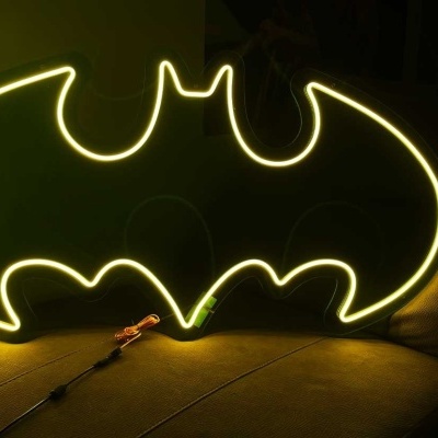 Neon LED decorativo símbolo Batman luz amarela sobre sofá cinzento