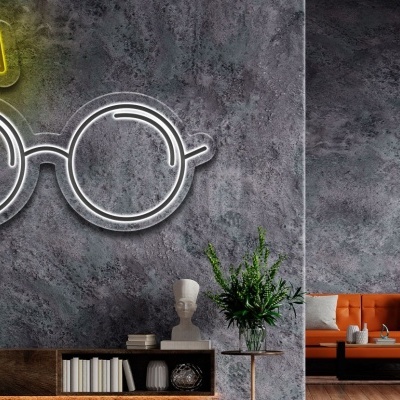 Interior de sala com parede cinzenta, luminária neón de óculos, sofá laranja e estante com livros e plantas