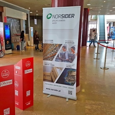 Expositor vermelho Caixaria OfKind e banner da empresa NORSIDER em espaço interior