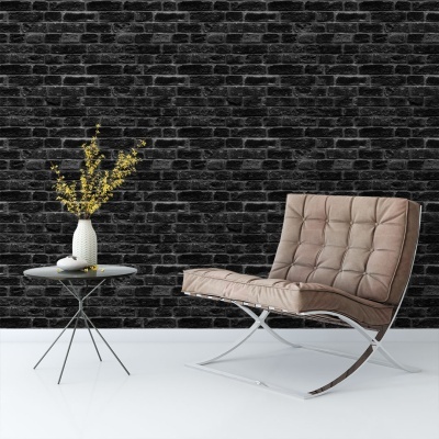 Cadeira estofada castanha junto a mesa com vaso branco e flores amarelas, parede tijolo preto