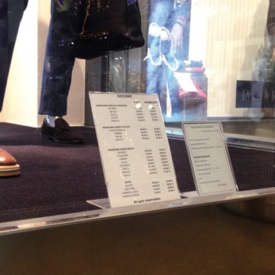 Vitrine de loja com calças e sapatos de pele em manequins e placas de preços