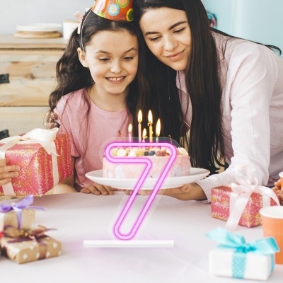 Meninas juntas ao redor de uma mesa branca com presentes e um bolo com vela número 7