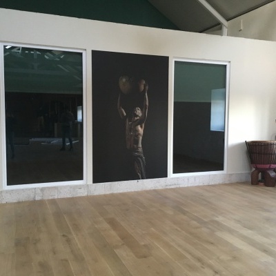 Três painéis com moldura branca, painel central com foto de homem a levantar criança, chão de madeira clara, instrumentos musicais à direita