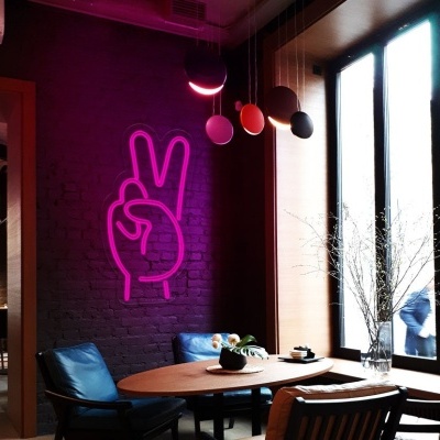 Interior de restaurante com mesa de madeira, cadeiras azul e preta, parede cinzenta com luz LED rosa em forma de mão, janela grande à direita