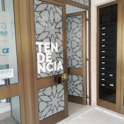 Porta de vidro com padrão floral e texto em letras brancas numa entrada de edifício