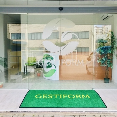 Entrada de escritório com portas de vidro, planta e tapete verde com texto GESTIFORM.