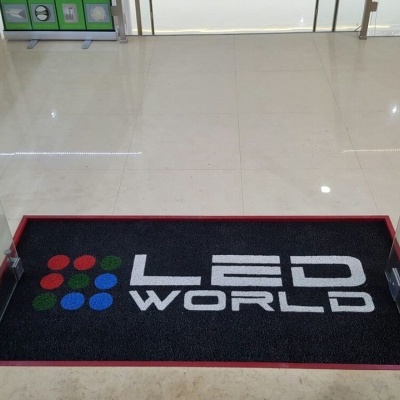 Tapete de entrada preto com logótipo LED WORLD colorido no chão de azulejo