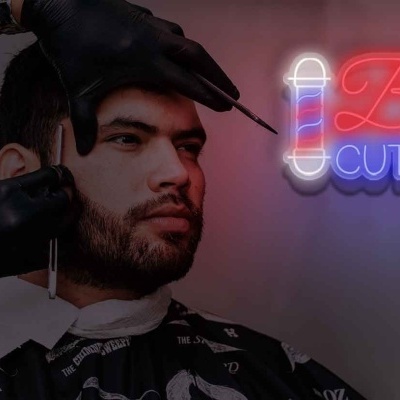 Homem a cortar cabelo com letreiro 'Barber CUT & SHAVE' neon ao fundo