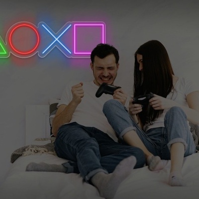 Casal sentado na cama a jogar videojogos com comandos e luzes de néon na parede