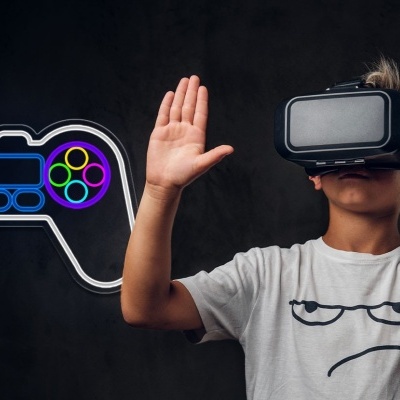 Criança com headset VR e t-shirt branca com rosto desenhado junto a imagem neon de comando videojogo