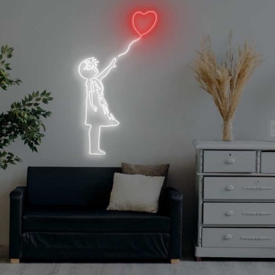 Sala de estar com sofá preto, néon de menina com balão, planta, cómoda branca e candeeiro de pé preto