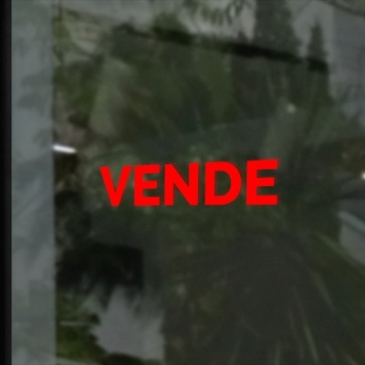 Placa vermelha com texto 'VENDE' em vidro refletindo árvores e interior com luz