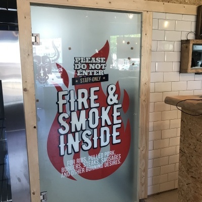 Porta de vidro fosco com texto e chamas vermelhas em restaurante