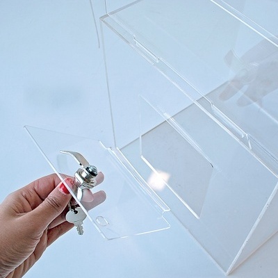 Caixa acrílica transparente com porta e fechadura prateada, mão segurando