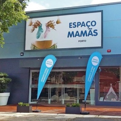 Fachada de loja Espaço Mamãs com sinal e bandeiras azuis e plantas no exterior.