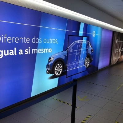 Painel publicitário com carro azul e texto em português num espaço interior
