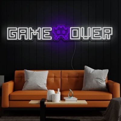 Neon decorativo GAME OVER com figura de pixel roxa, parede preta, sofá laranja com almofadas cinzentas, mesa de centro com objetos