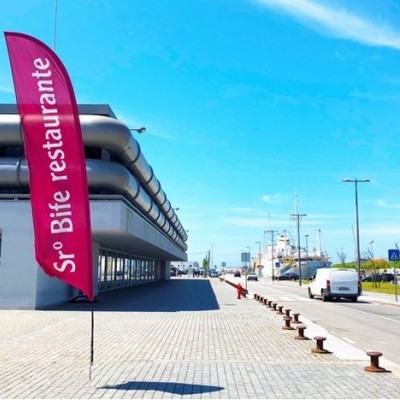 Bandeira rosa de restaurante perto de edifício moderno cinzento e rua com carros