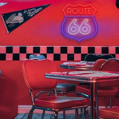 Restaurante com decoração retro vermelho e preto, cadeiras e mesas, letreiro ROUTE 66 e discos de vinil na parede
