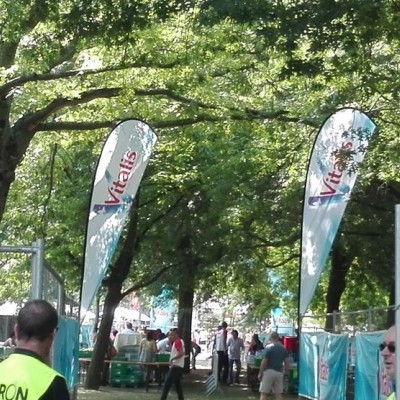 Bandeiras publicitárias Vitaïs ao ar livre com pessoas e árvores ao fundo