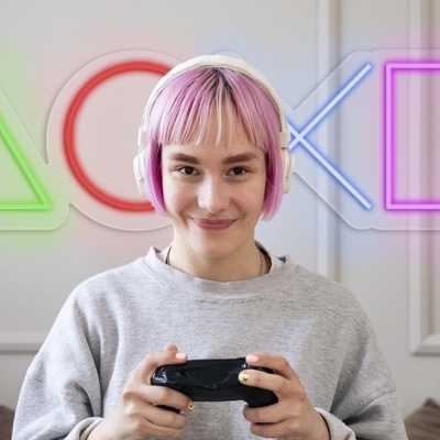 Pessoa com cabelo rosa a usar auriculares e a segurar comando de jogo com símbolos de controle em néon ao fundo