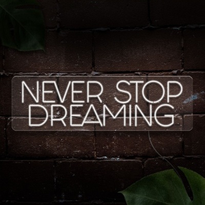 Placa de acrílico com letras em néon branco 'NEVER STOP DREAMING' na parede de tijolos vermelhos