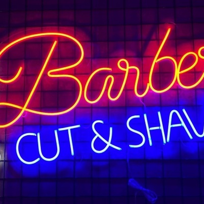 Letreiro de néon colorido com texto 'Barber CUT & SHAVE' e símbolo de barbeiro
