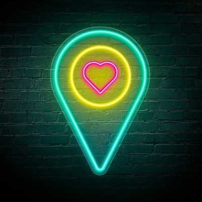 Neon em forma de marcador de localização com coração no centro, sobre parede de tijolos escura