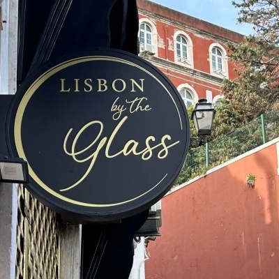 Placa redonda preta com texto dourado LISBON by the Glass pendurada numa parede externa