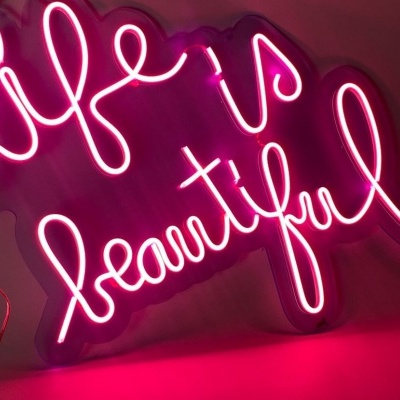 Letreiro neon rosa com a frase 'life is beautiful' em fundo escuro
