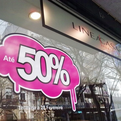 Placa promocional Até 50% na vitrine de loja com reflexo de árvores e edifícios