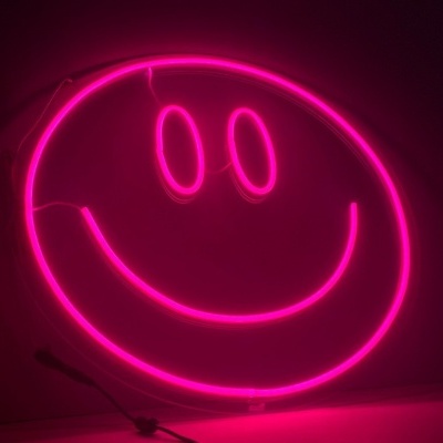 Neon rosa smiley face contra parede branca em ambiente escuro