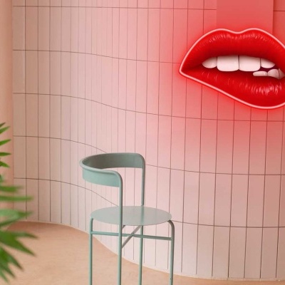 Espaço interior com parede rosa, cadeira azul clara, néon lábios vermelhos e planta verde