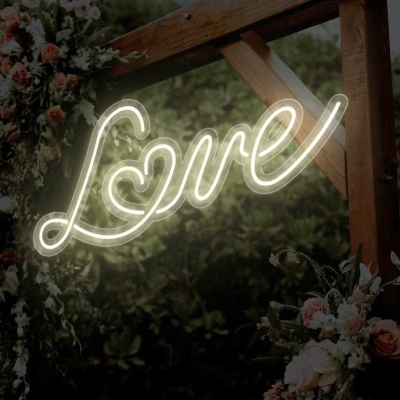 Sinal de néon 'Love' pendurado numa estrutura de madeira com flores ao ar livre