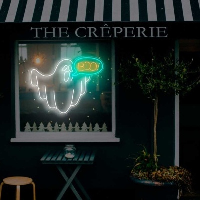 Fachada de creperia com toldo verde e branco, letreiro luminoso, quadro negro com menu e plantas