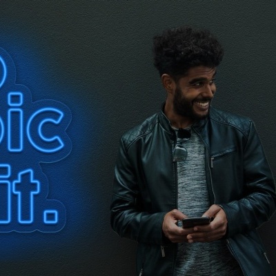 Homem sorridente com casaco de couro preto e letreiro neon azul com 