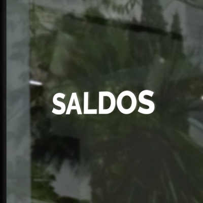 Palavra SALDOS em letras brancas numa porta de vidro com reflexo de planta e escada