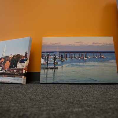 Três quadros com imagens marítimas apoiados no chão junto a uma parede laranja.