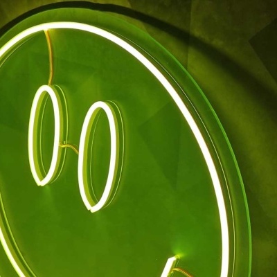 Sinal de néon verde com rosto sorridente iluminado sobre fundo geométrico