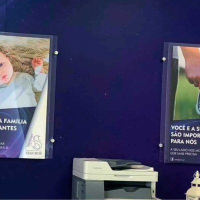 Painéis publicitários com imagens e texto em português sobre saúde, numa parede azul escura, com uma impressora e luminária em baixo.