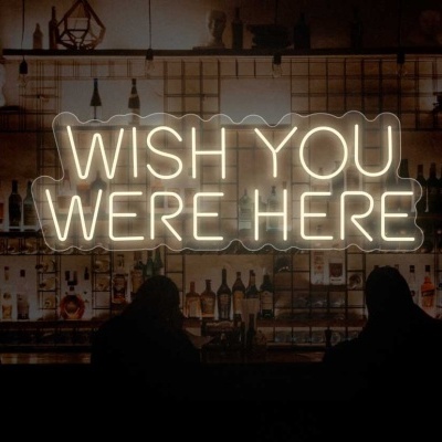 Sinal de néon branco 'WISH YOU WERE HERE' numa parede de azulejos brancos num bar