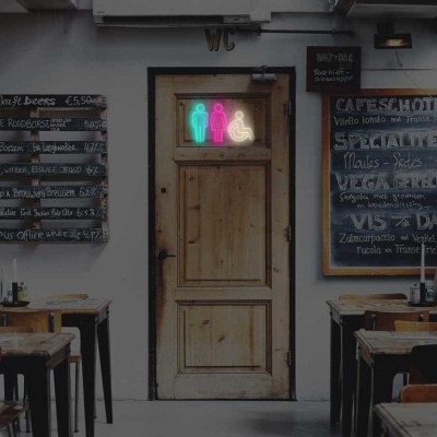Interior de café com mesas e cadeiras de madeira, quadros-negros e porta de madeira com letreiro luminoso