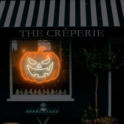 Fachada da creperia THE CRÊPERIE com toldo às riscas e decoração luminosa de abóbora