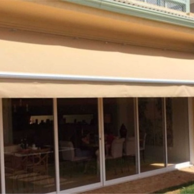 Toldo bege claro em varanda com porta de vidro deslizante e jardim