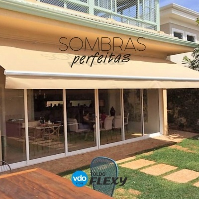 Toldo bege claro com texto SOMBRAS perfeitas instalado numa casa com jardim