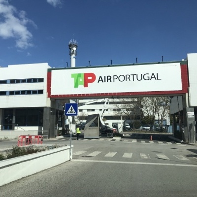 Entrada de acesso com letreiro TAP AIR PORTUGAL e edifícios ao fundo