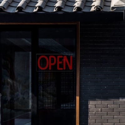 porta de vidro com letreiro OPEN vermelho e parede de tijolos escuros