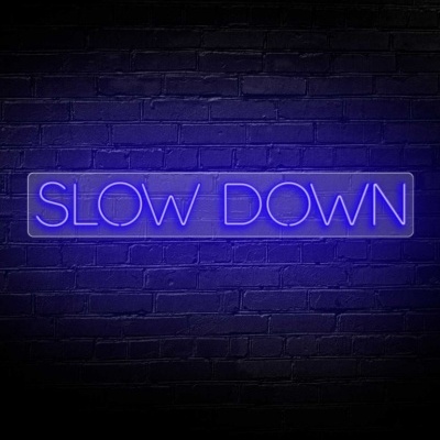 Placa de néon azul SLOW DOWN numa parede de tijolos preta
