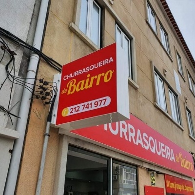 Placa vermelha com texto CHURRASQUEIRA do Bairro num edifício.