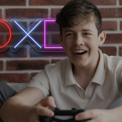 Jovem com comando de videojogo em frente a parede de tijolos com símbolos coloridos de videojogo